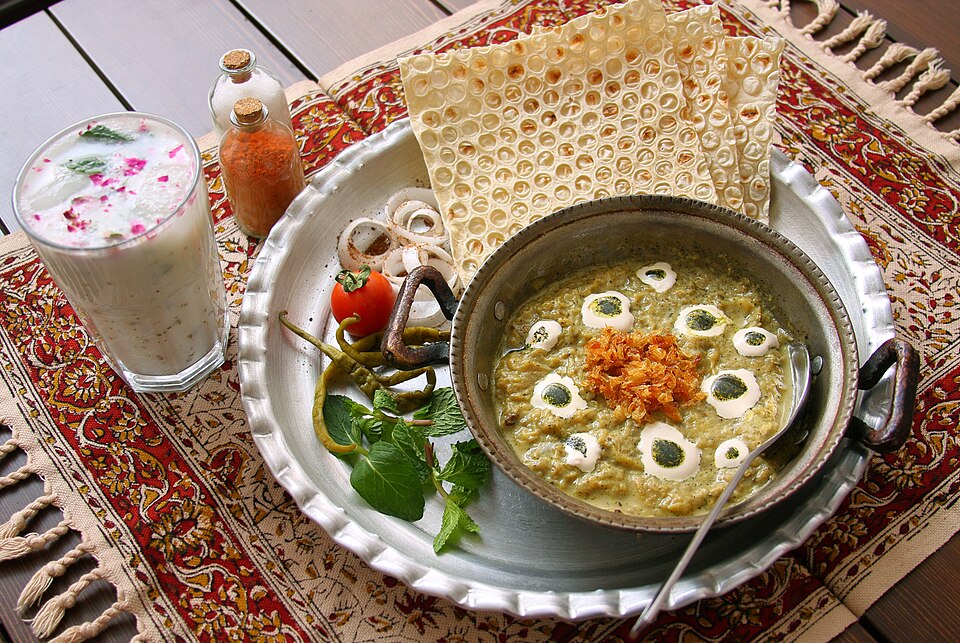 A glass of Iranian doogh served with kashk-e bademjan and Persian bread in Iran