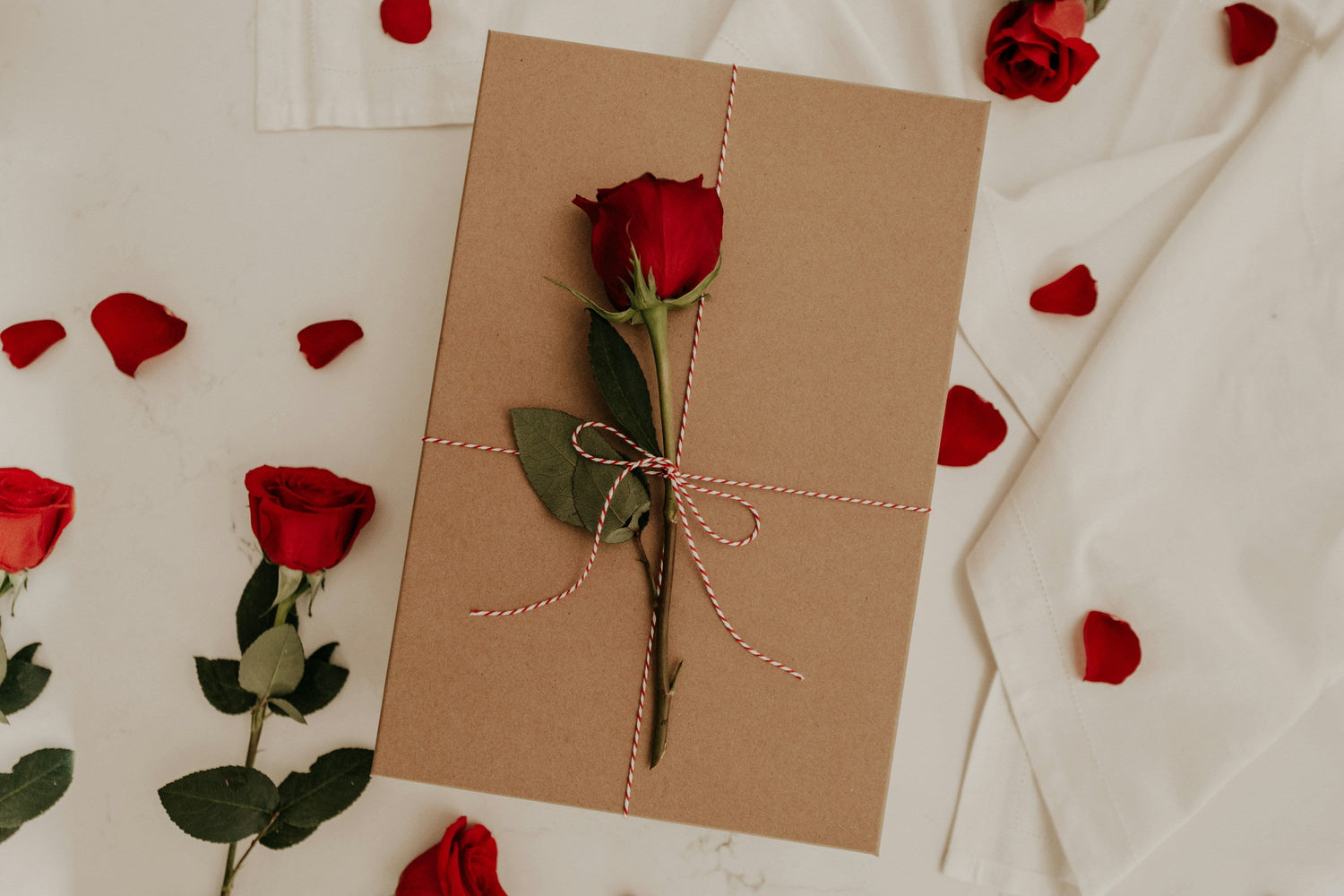 Valentine’s gift box decorated with a red rose and petals on a soft beige background.